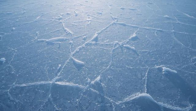 Frozen pond geometry with polygonal ice cracks and frost ridges shimmering blue stillness