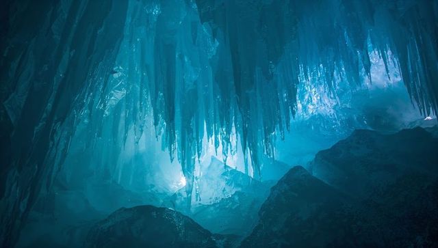 Blue glacial ice cave with dramatic icicle stalactites and ethereal teal light underground