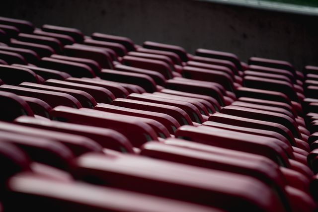 The image portrays rows of empty red stadium seats in an outdoor venue. This could be used to depict sports, concerts, or events, offering visuals for tickets, arenas, seating charts, or background designs.