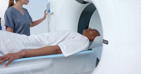 Male patient lying in ct scanner while technician operating touchscreen controls for medical imaging