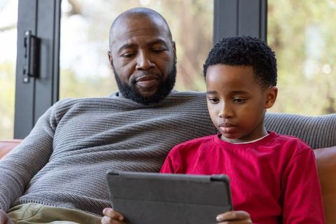 African American father and son bonding while using tablet together on home sofa