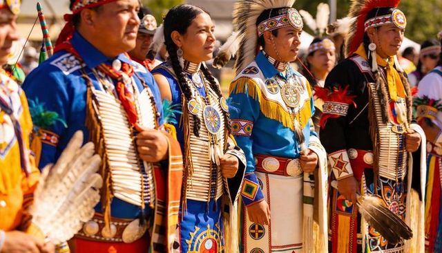 Indigenous dancers wearing fringed regalia and beadwork during powwow procession outdoors