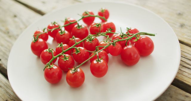 Captured image showing freshly picked cherry tomatoes on a simple white plate laid on wooden table, emphasizing freshness and color contrast. Perfect for promoting healthy eating, organic farming, diet plans, culinary blogs, and kitchen decor themes.