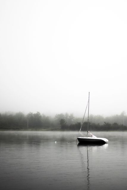 Sailboat anchored on calm misty lake reflecting on the water, creating a tranquil and serene atmosphere. Perfect for projects focusing on concepts like solitude, peace, and nature's beauty. Ideal for wall art, meditation aids, coastal-themed decor, or as a background in digital design.