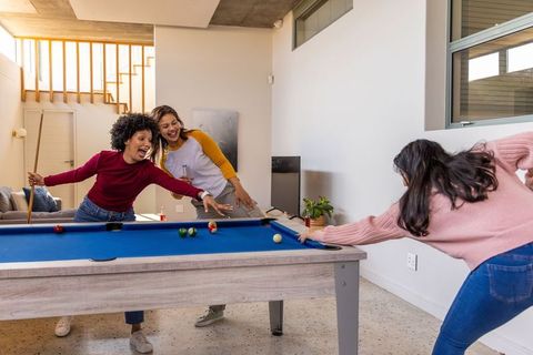 Three friends playing pool on blue-felt table in modern midcentury home
