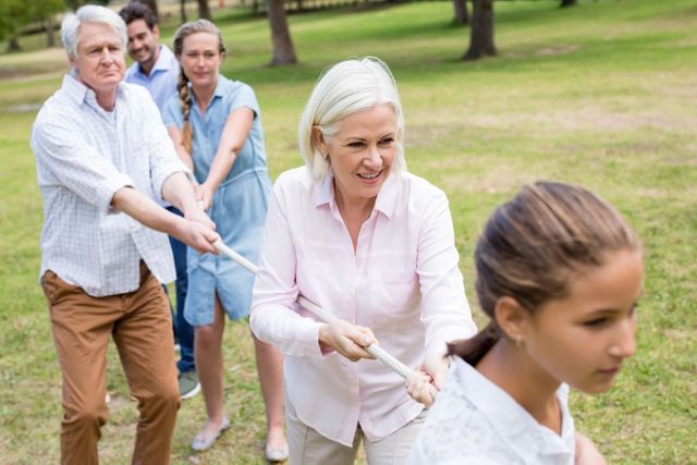 Multi-generational family engaging in a friendly tug of war in park. Suitable for illustrating family bonding, outdoor activities, teamwork, and summer fun. Perfect for advertisements, blogs, and articles about family activities, health, and fitness.