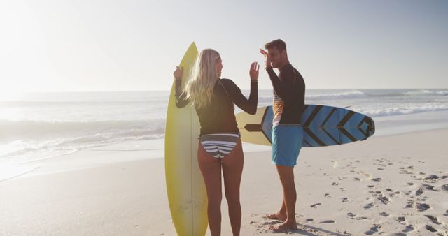 Surfer couple stands on beach with surfboards, getting ready to enter the waves at sunrise. Ideal for representing outdoor activities, surfing culture, adventure travel, and ocean-related content.