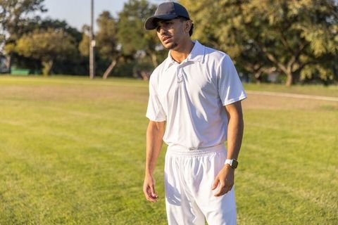 Indian athlete standing on cricket field wearing white uniform and cap at golden hour
