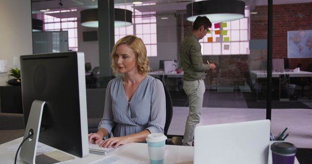 Caucasian businesswoman working on laptop with biracial colleague in background using memo notes. business in a modern office.