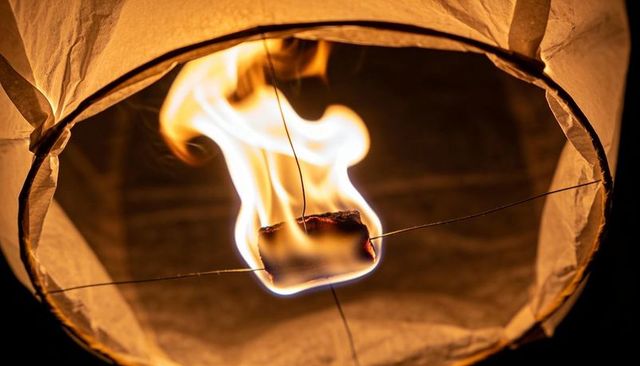 Burning fuel cell inside paper sky lantern glowing flame close-up at night festival celebration