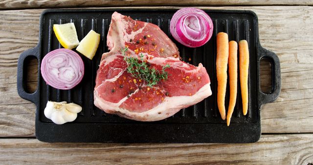 Raw steak seasoned with spices is ready for cooking on a cast iron grill pan, accompanied by fresh vegetables and herbs. The arrangement showcases a preparation for a flavorful and nutritious meal.
