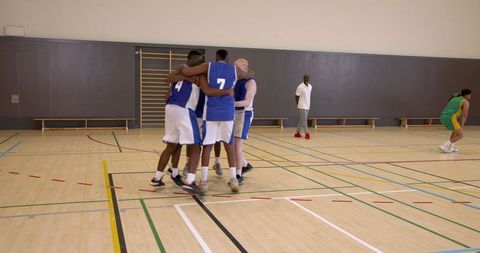 Diverse male basketball team celebrating victory at gym midcourt