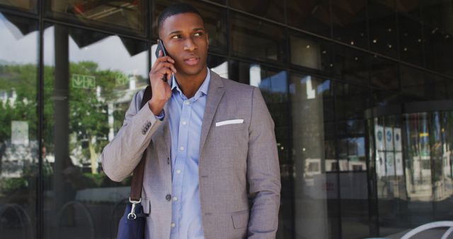 This image shows a professional businessman talking on a smartphone while standing outside an office building. Perfect for use in articles about business communication, corporate life, and urban professional style. It is particularly suited for financial, consulting, and tech industries' websites and marketing materials.