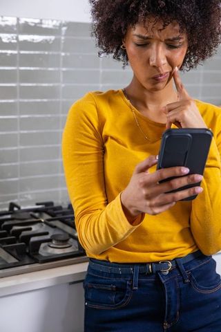 Woman contemplating message on smartphone in kitchen
