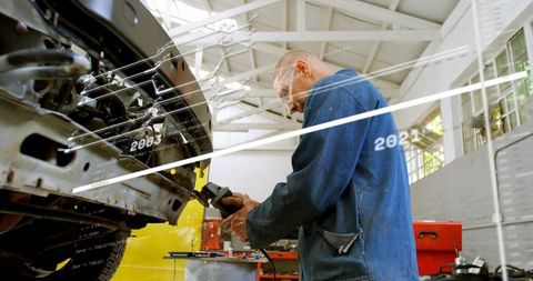Bald mechanic grinding front chassis with angle grinder in bright workshop with skylights