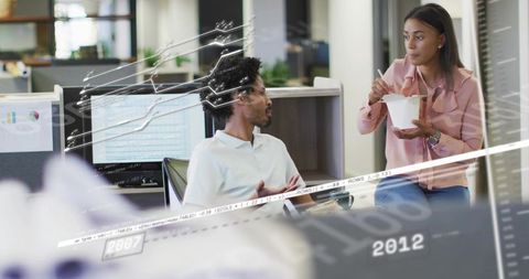 Two coworkers discussing data while eating lunch at open office with overlaid analytics