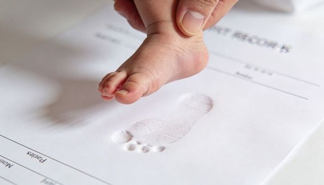 Pressing newborn foot onto registration form for birth record, caregiver guiding footprint