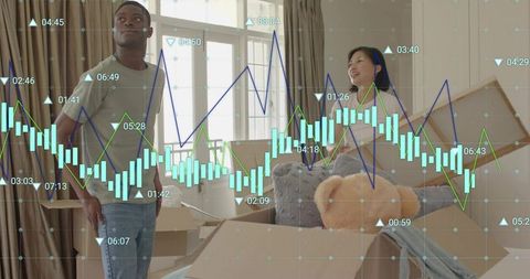 Young couple unpacking moving boxes in sunlit apartment with stock market data overlay