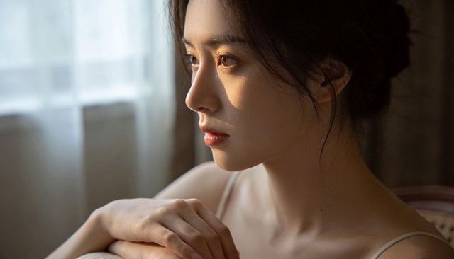 Serene woman gazing through window with warm morning light and sheer curtains