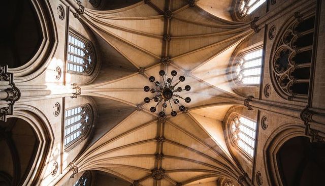 Golden sunlit gothic vaulted ceiling featuring ornate multi-arm chandelier and tracery