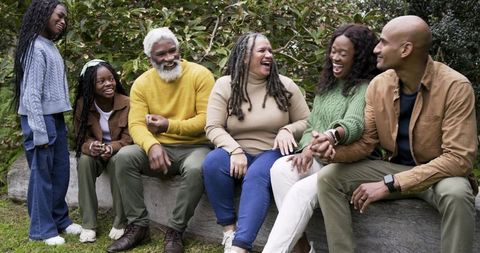 Multigenerational diverse family laughing together on log bench in green park gathering