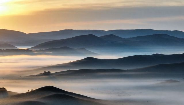 Misty rolling hills at sunrise: layered ridges, fog-filled valleys and golden glow
