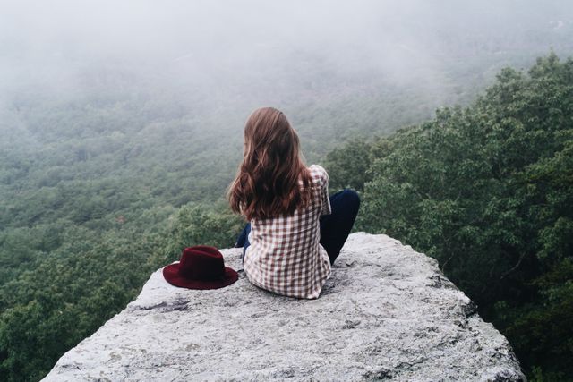 Woman Sitting on Edge of Cliff Overlooking Foggy Forest - Download Free Stock Photos Pikwizard.com