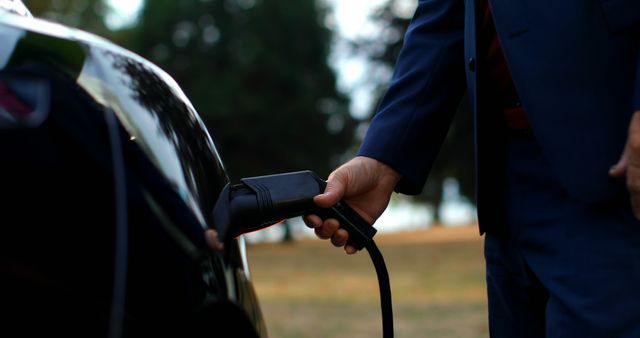 Person plugging in an electric car charger outdoors. Ideal for themes related to electric vehicles, sustainable transportation, and green technology. Useful for articles, advertisements, and campaigns about eco-friendly driving and renewable energy.