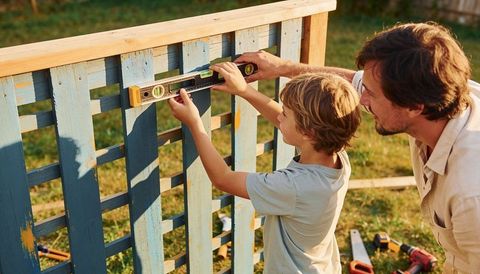 Father teaching son using spirit level on painted backyard fence during weekend diy
