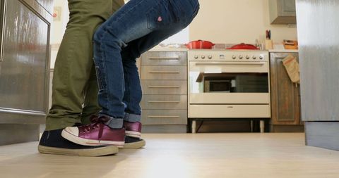 Child Stretching Up on Tiptoes to Reach Parent in Cozy Kitchen