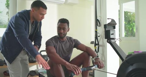 Trainer coaching client on rowing machine during guided home fitness workout session