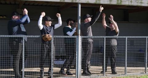 Baseball teammates cheering in shaded dugout while wearing caps and glove on belt