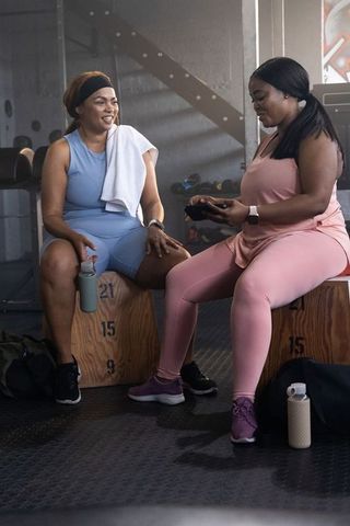 Multiracial women resting on plyo boxes, checking fitness app, smiling after workout