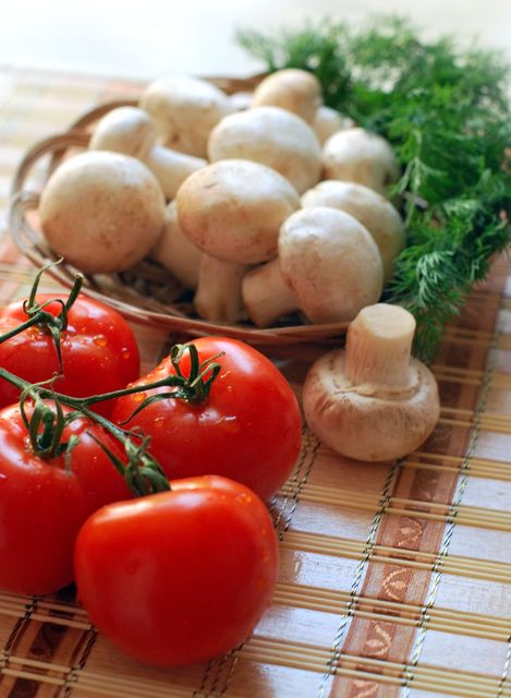 Fresh tomatoes and mushrooms are displayed on a bamboo mat with a basket, complemented by a sprig of parsley. This image is suitable for promoting healthy food blogs, cooking websites, recipe books, dietary guides, farmers' markets, and organic food stores. The natural setting emphasizes the freshness and organic quality of the produce, perfect for culinary and lifestyle content.