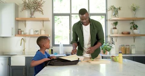 African american father preparing snack while son packing backpack at kitchen island