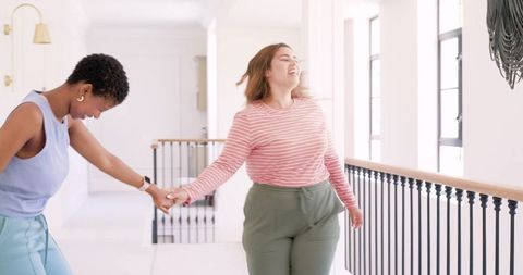 Two african american women walking and laughing hand-in-hand in bright minimal hallway