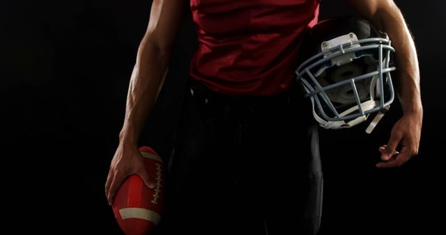 Image shows a football player holding a helmet and ball against a dark background. Ideal for use in sports advertising, articles on American football, training material, fitness promotions, and sportswear branding.