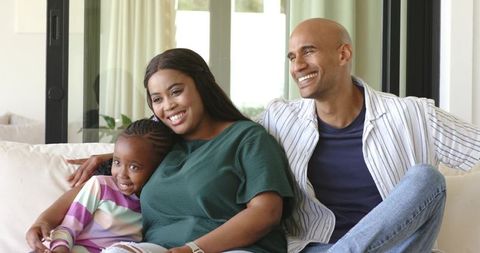 Multicultural family relaxing on sofa, parents and child cuddling and smiling at home