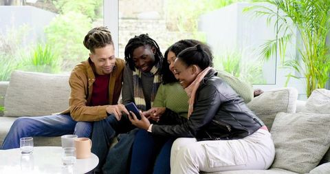 Diverse friends sharing smartphone laughter on bright modern living room sofa