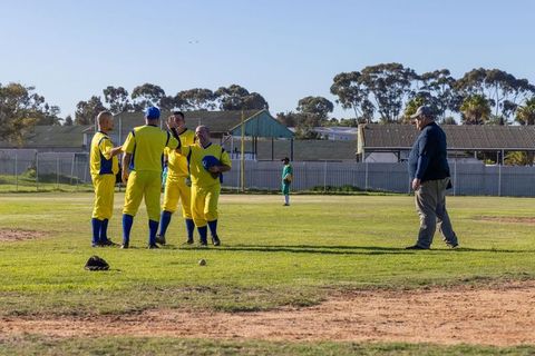 Umpire approaching while yellow team celebrating softball run on sunny baseball field