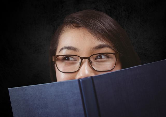 This image depicts a woman wearing glasses, holding a book in front of her face against a dark background. Her thoughtful expression suggests deep contemplation or focus. This image can be used for educational content, book covers, learning materials, or articles related to reading and knowledge.