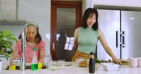 Mother and daughter joyfully washing dishes together at modern kitchen