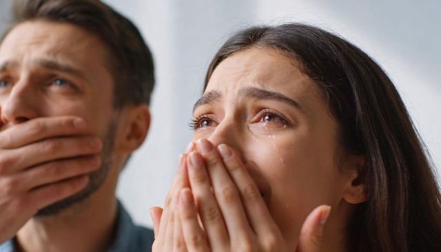 Emotional couple reacting in shock with crying woman and man covering mouth, closeup