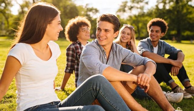 Young friends chatting and laughing while sitting on sunny park grass