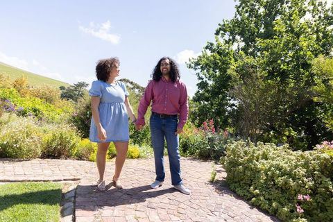 Couple Holding Hands in Sunny Garden Surrounded by Lush Greenery