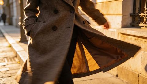 Adult walking in double-breasted wool coat flare revealing lining on urban sidewalk at golden hour
