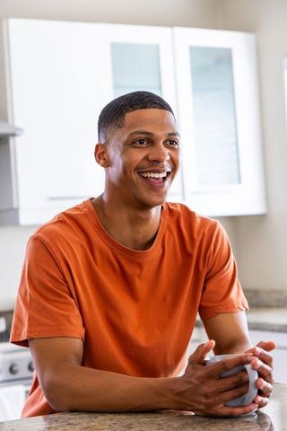 Young african american man smiling with coffee at modern kitchen counter, casual morning lifestyle