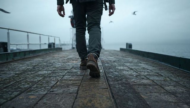 Traveler walking toward foggy horizon on wet pier with backpack and seagulls