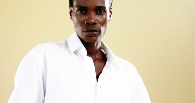 This photograph features an African American woman confidently looking at the camera, wearing a white shirt. The neutral background complements the subject. Ideal for use in fashion magazines, advertising themes of confidence and empowerment, or beauty blogs.