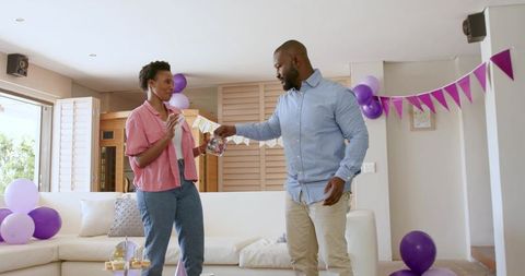 African American couple exchanging candy jar while decorating living room for birthday